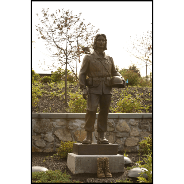photo of bronze-colored sculpture of soldier in garden setting with rock wall behind