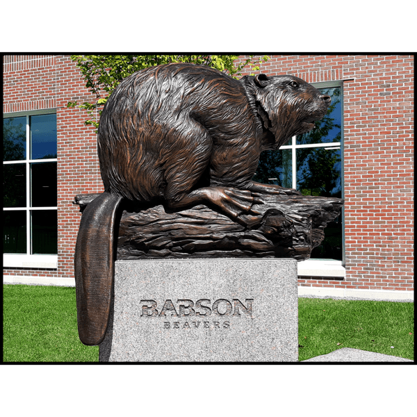 photo of bronze sculpture of beaver on log on granite base in front of brick building