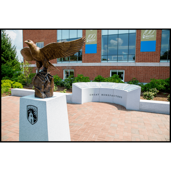 photo of bronze sculpture of eagle with wings open on rocky surface on top of granite base surrounded by other stonework in brick plaza in front of a brick building
