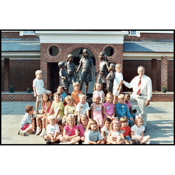 photo of children and sculptor Robert Shure with bronze sculpture of five children standing in half circle holding hands atop brick-faced pedestal