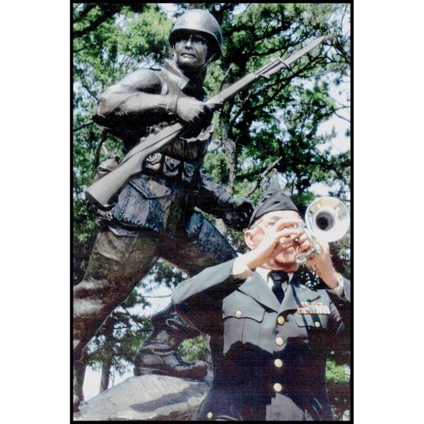 photo of bronze-colored sculpture of soldier holding rifle in action on incline with trees behind and veteran in dress uniform in front playing trumpet