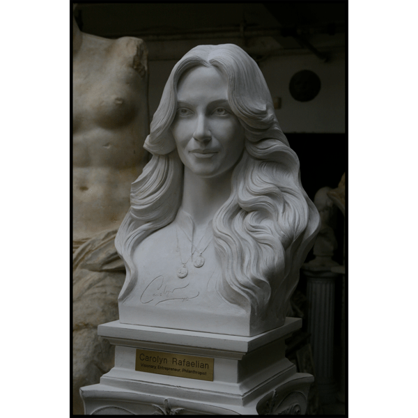 photo of white-colored sculpture bust of Carolyn Rafaelian on white square base with small gold-colored plaque on ornate white pedestal in a room with white statues behind