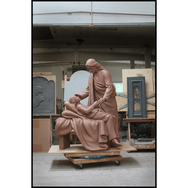 clay model of sculpture of Jesus Christ figure leaning over sick child on bed in sculpture studio
