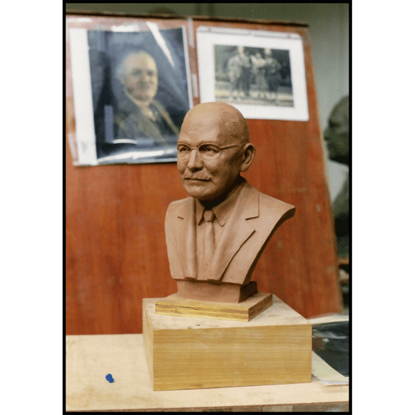 photo of clay model of sculpture bust of Donald Ross on wood blocks on wood work table with reference photos on board behind