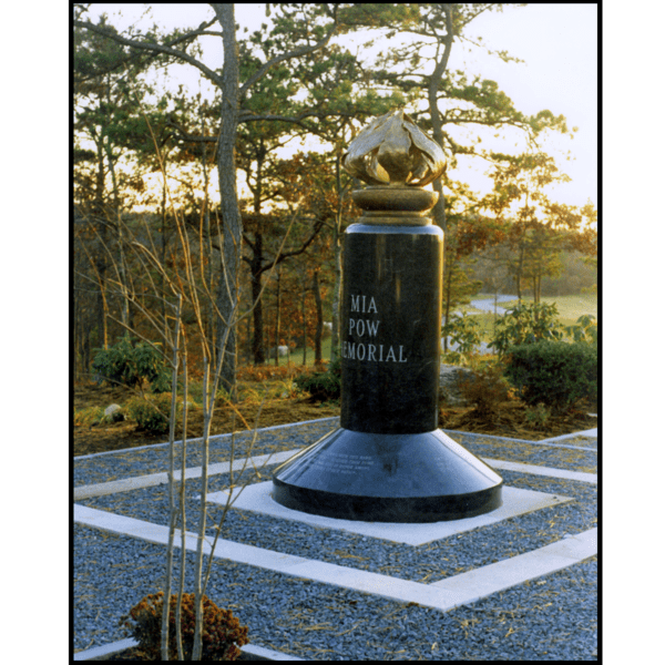 photo of bronze sculpture of flame on black granite base with inscriptions in hardscaped area with surrounding trees and greenery