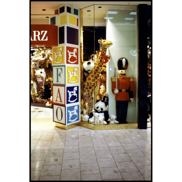 photo of FAO Schwarz toy store front window with logo tower of blocks, stuffed animals, and polychromed toy soldier sculpture