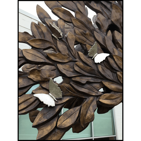 closeup photo of bronze-colored tree sculpture with silver-colored sculpted butterflies and building in background