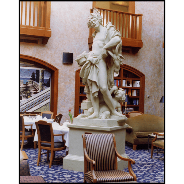 photo of white-colored sculpture of male and child half-clothed atop white-colored pedestal in room with blue carpet and wooden tables, chairs, bookshelves, and wood-trimmed doorways