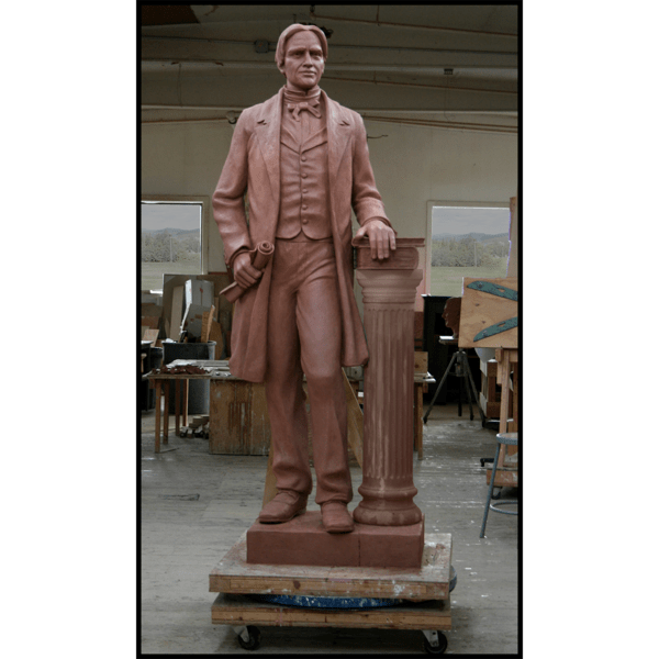 photo of clay model of statue of Horace Mann holding scroll and standing beside column with books in sculpture studio