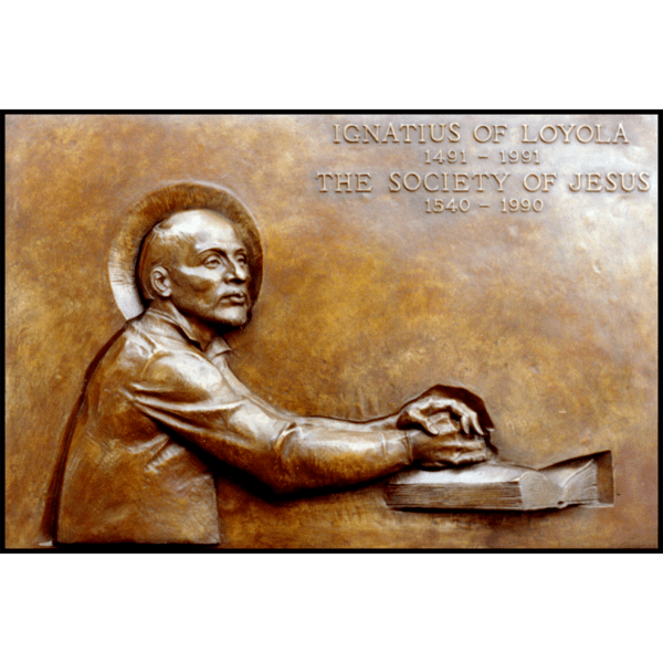 photo of bronze-colored plaque with relief of Ignatius of Loyola with hands folded on a book