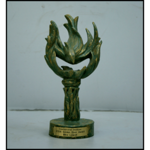 photo of green-colored sculpture of abstract bird flying downward onto torch-like shape on a base with plaque