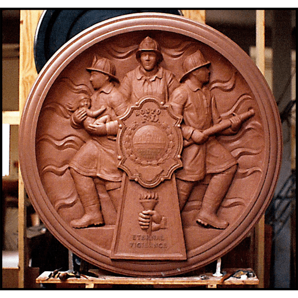 photo of clay model of relief sculpture plaque honoring Boston Firefighters with three firefighters and large fire department badge at sculptor's studio
