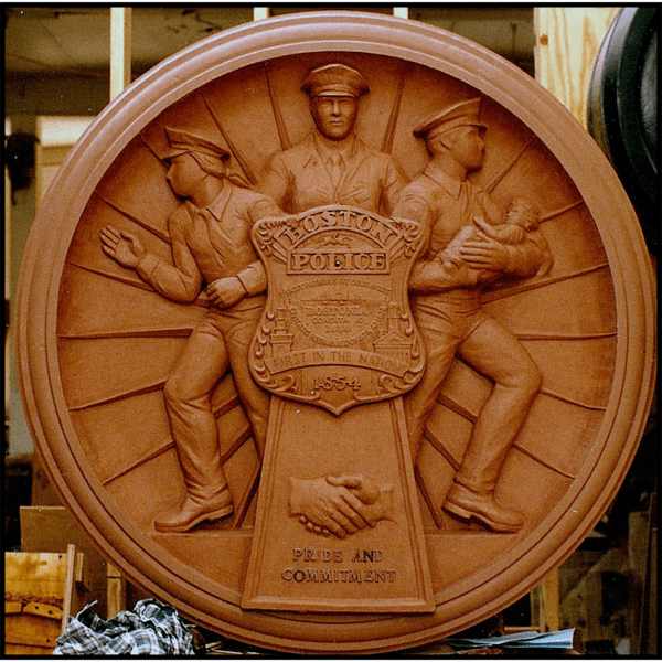 photo of clay model of relief sculpture plaque honoring Boston Police with three officers and large police badge at sculptor's studio