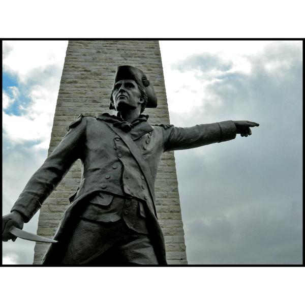 exterior photo of bronze sculpture of John Stark pointing with outstretched arm in front of a obelisk-type monument