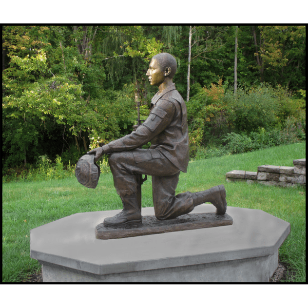 exterior photo of bronze sculpture of Johnny Roberge kneeling and in uniform on concrete base in a park