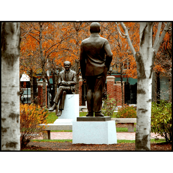 photo of bronze statues of Morris Gaebe and Edward Triangolo on college campus with fall foliage