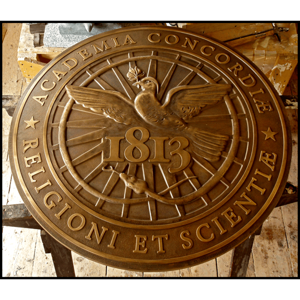 photo of bronze-colored sculpted relief of Kimball Union Academy seal featuring bird, snake, and Latin text in sculptor's studio