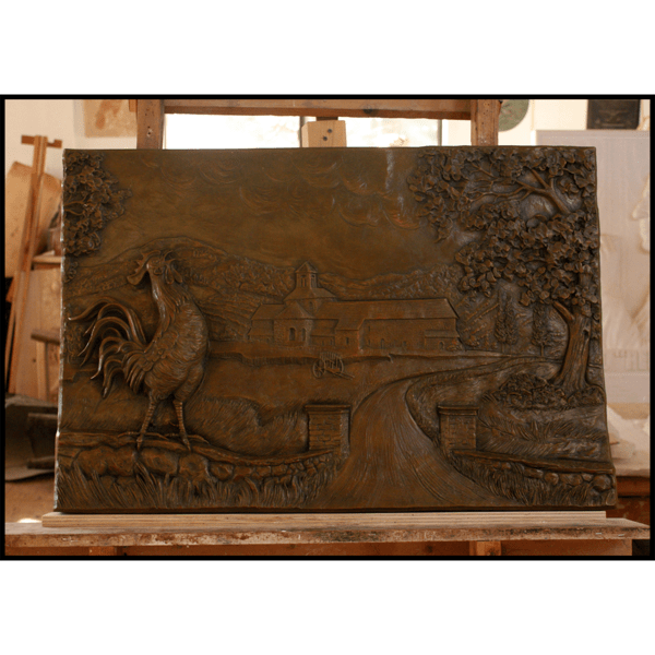 photo of bronze-colored relief plaque of farmhouse with rooster and tree in foreground in sculptor's studio