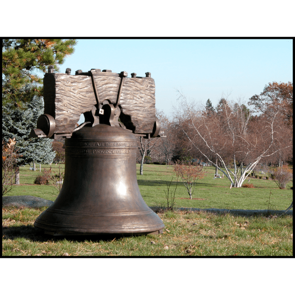 photo of bronze-colored Liberty Bell with yoke in field with trees in background