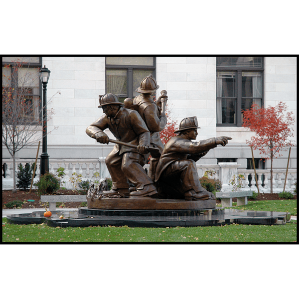 photo of bronze sculpture of three firefighters in action stances on a stone base in front of white stone building with grass in foreground