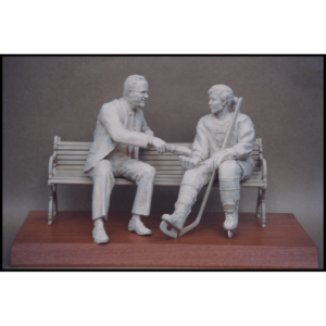 photo of white-colored sculpture of George Matthews on bench with a female in hockey gear atop a wood base