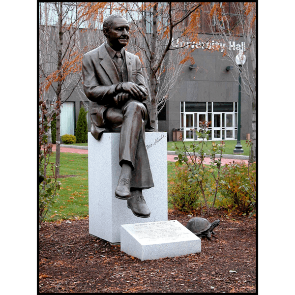 photo of bronze statue of Morris Gaebe sitting on stone base on college campus