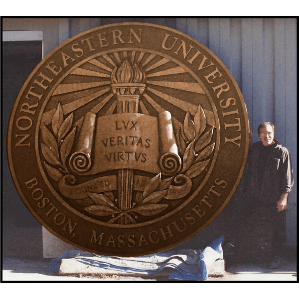 photo of bronze relief sculpture of Northeastern University's seal leaning up against wall with artist Robert Shure beside it