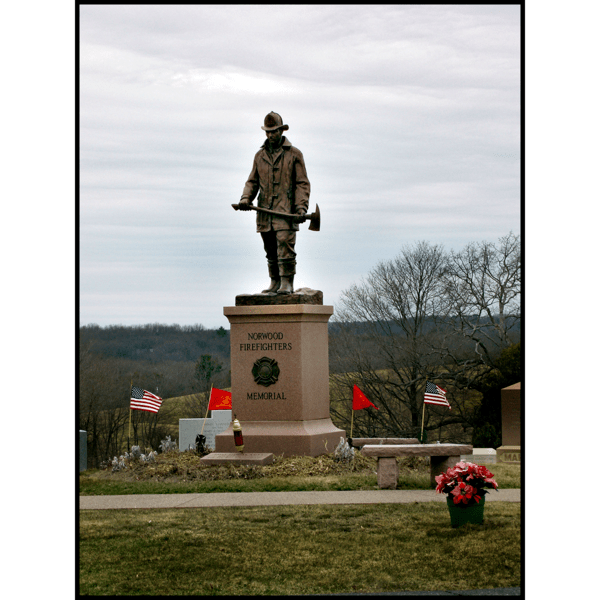 photo of bronze statue of standing firefighter holding an ax atop a tall stone base in a cemetery