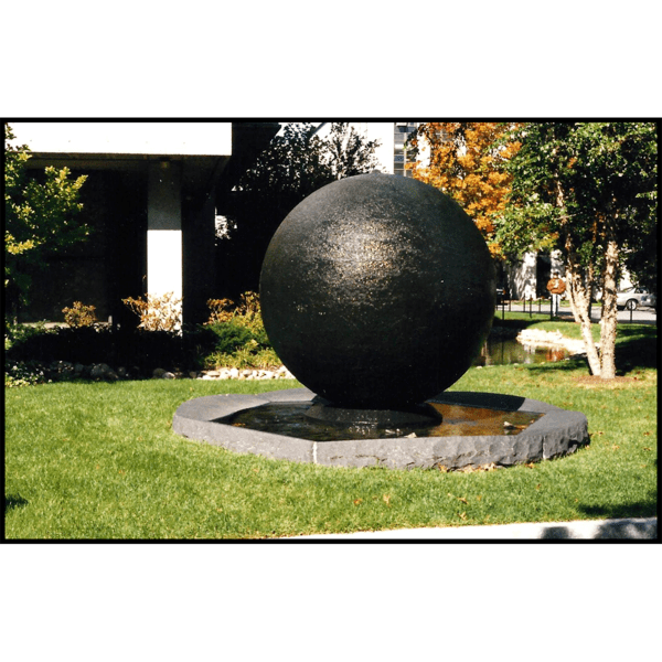 photo of black-colored sphere in stone-rimmed pool of water surrounded by landscaping and buildings