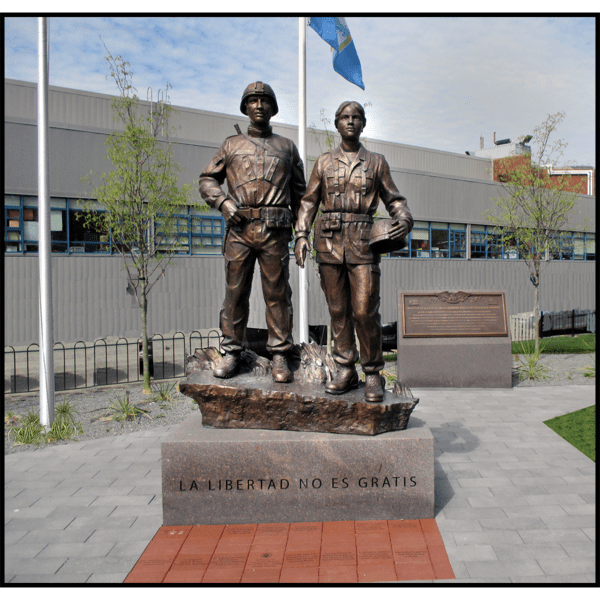 photo of bronze sculpture of two soldiers standing next to one another on low base with paving around them and building in background