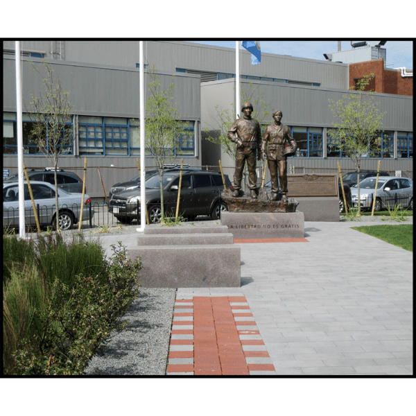 photo of bronze sculpture of two soldiers standing next to one another on low base with paving around them and building in background