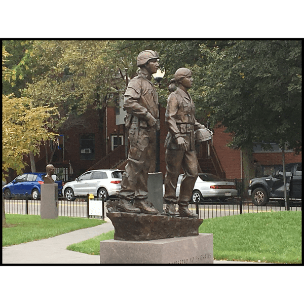 photo of bronze sculpture of two soldiers standing next to one another on low base with paving and lawn around them