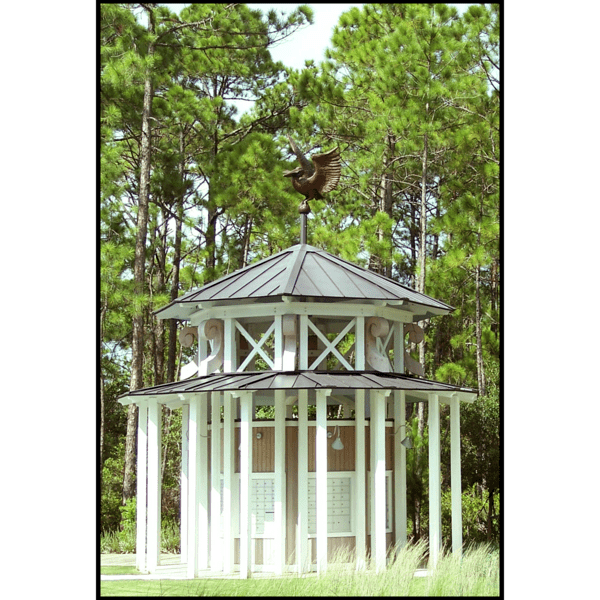 photo of gazebo-like mail kiosk with brown roofs and white supports topped with a bronze sculpture of a pelican with letter in beak and surrounded by trees and grass