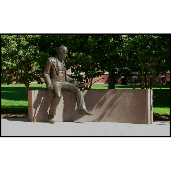 photo of bronze sculpture of Sigmund Freud sitting on a stone bench in a plaza with trees and grass behind