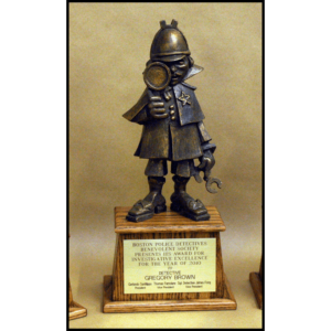 photo of bronze-colored sculpture of cartoon-like police detective atop a wood base with a plaque
