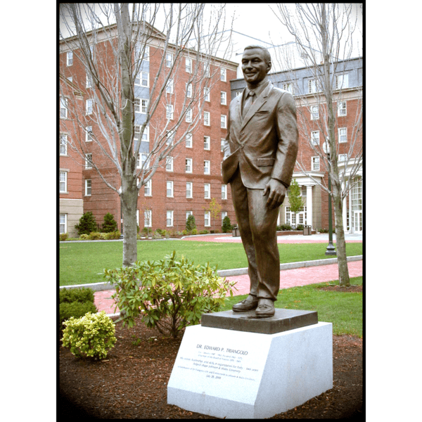 photo of bronze statue of Edward Triangolo standing on stone base on college campus