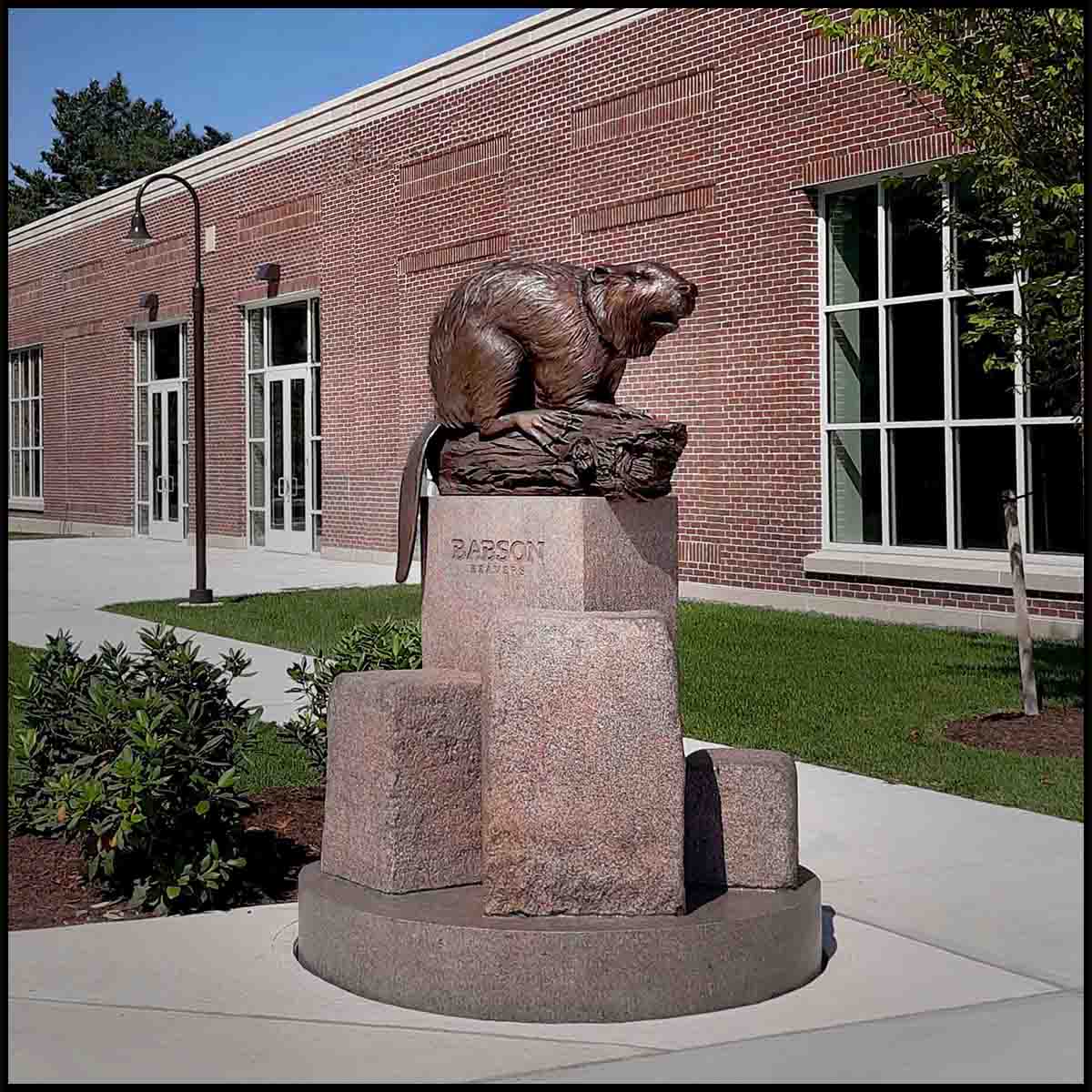 photo of bronze sculpture of beaver on log on granite base made of geometric and natural shapes in front of brick building