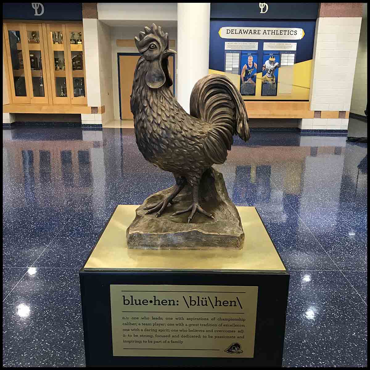 photo of bronze sculpture of hen on black and gold base in large room with blue floor