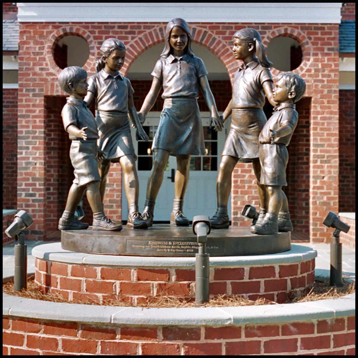 photo of bronze sculpture of five children standing in half circle holding hands atop brick-faced pedestal