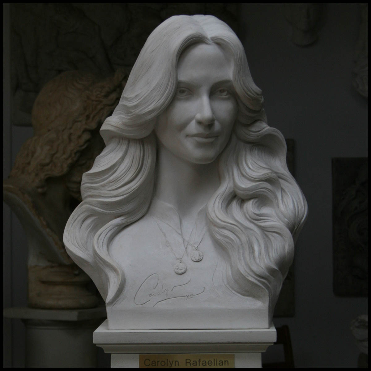 photo of white-colored sculpture bust of Carolyn Rafaelian on white square base with small gold-colored plaque against a black background