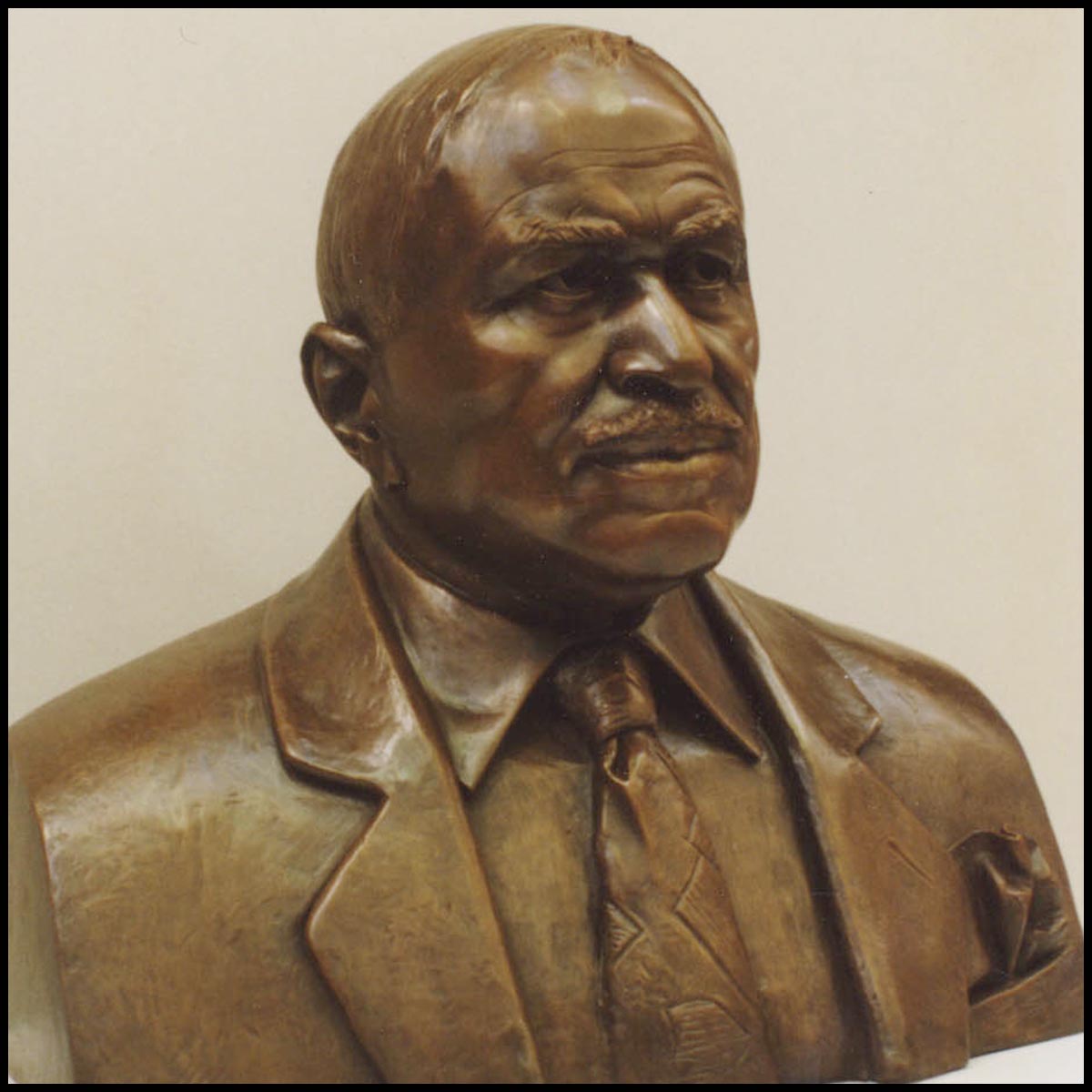 photo of bronze-colored sculpture bust of Eddie Robinson wearing suitcoat and tie against tan background