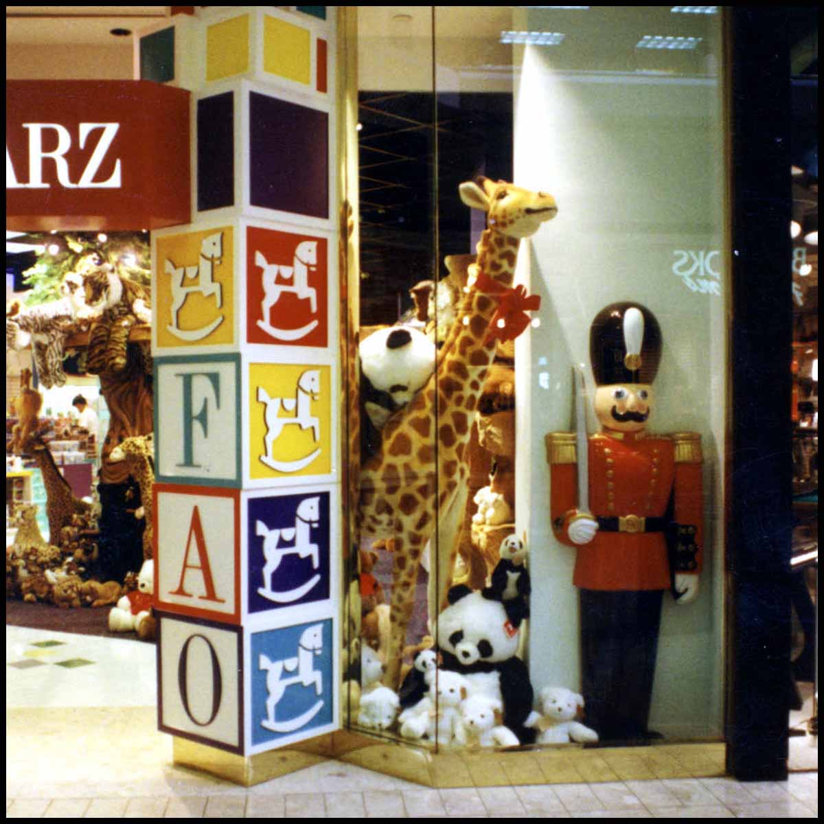 photo of FAO Schwarz toy store front window with logo tower of blocks, stuffed animals, and polychromed toy soldier sculpture