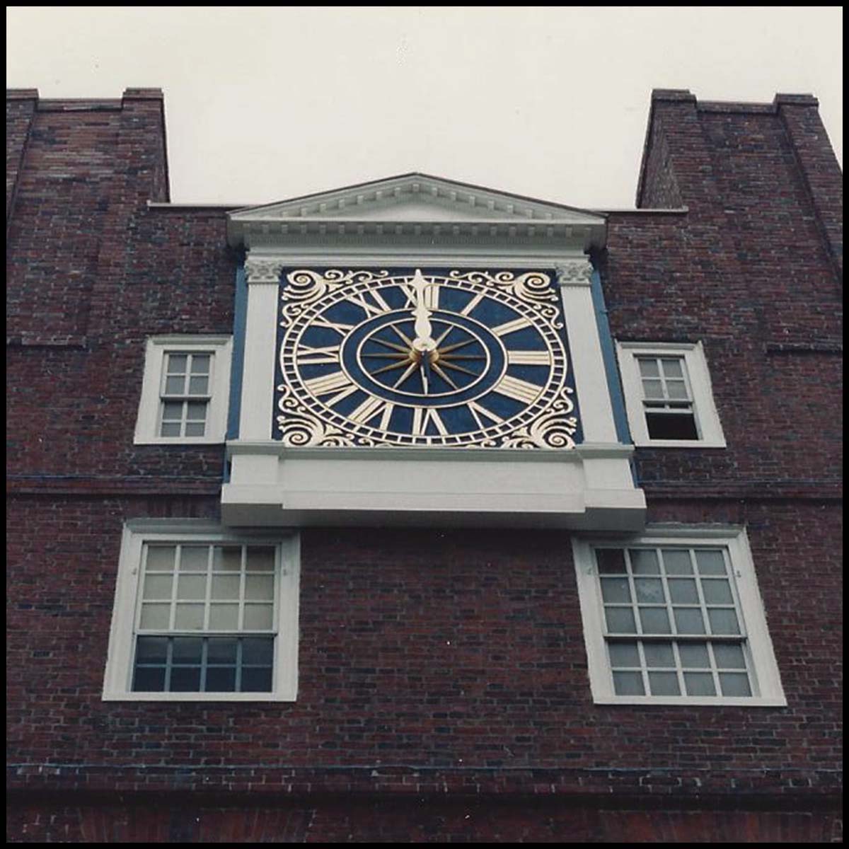 photo of blue and gold clock topped with pediment on a brick building