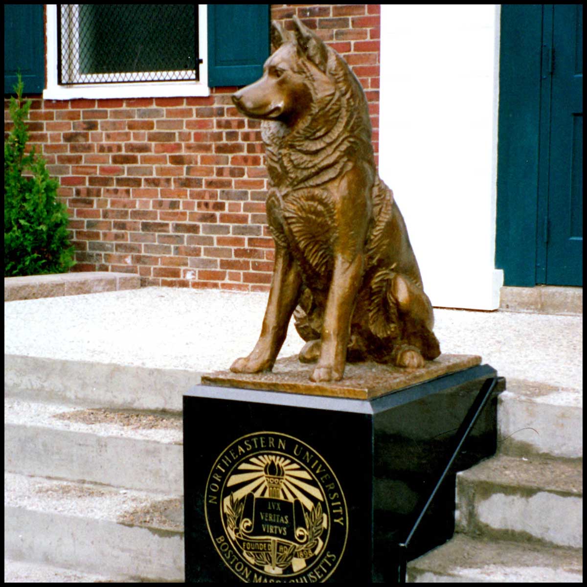 photo of bronze-colored sculpture of seated husky on black base with school logo on staircase