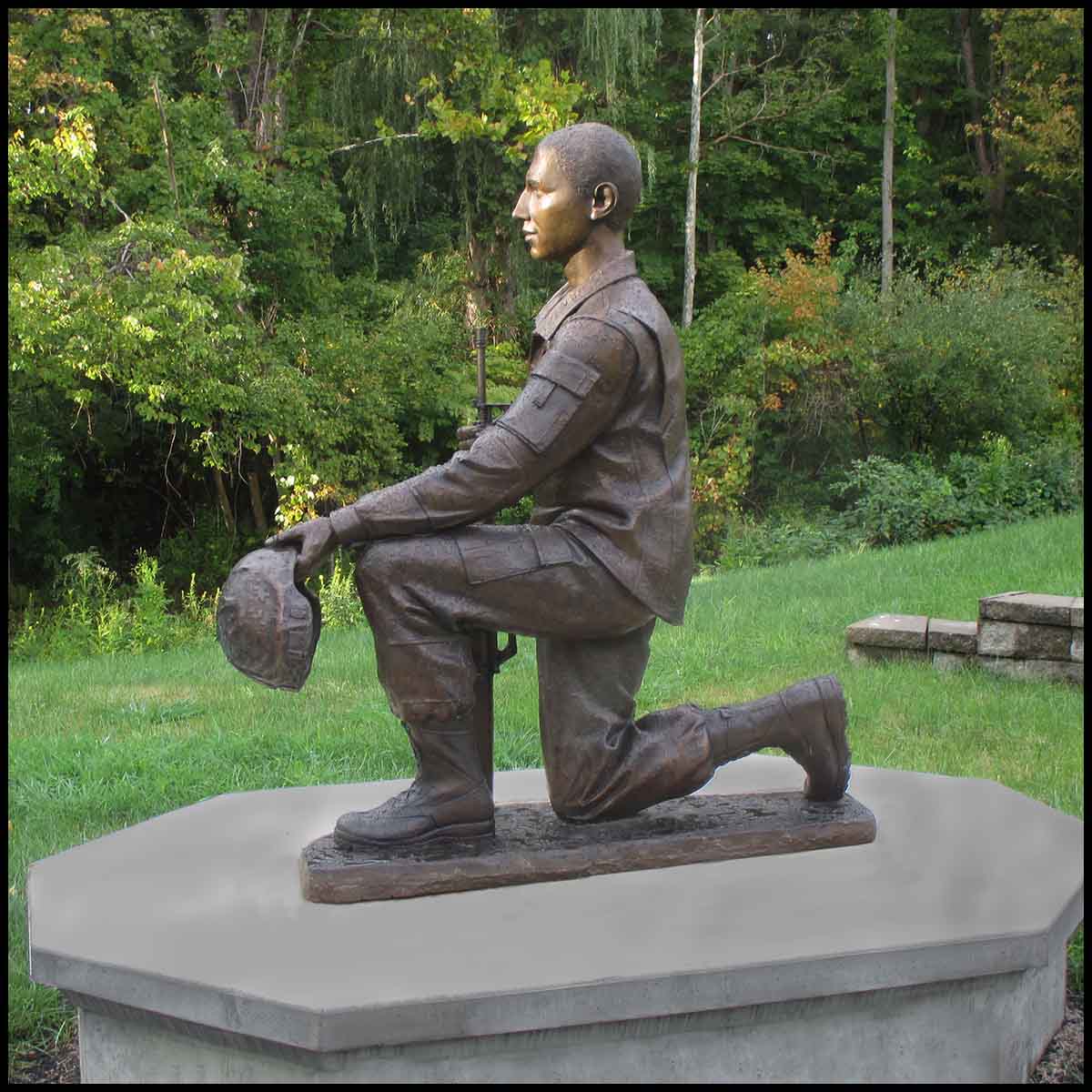 exterior photo of bronze sculpture of Johnny Roberge kneeling and in uniform on concrete base in a park