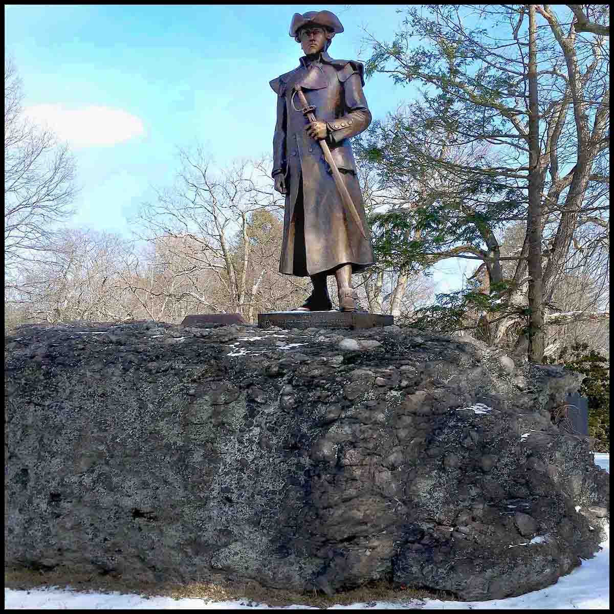 photo of bronze statue of Joseph Warren in uniform holding sword hilt at his side atop a large puddingstone