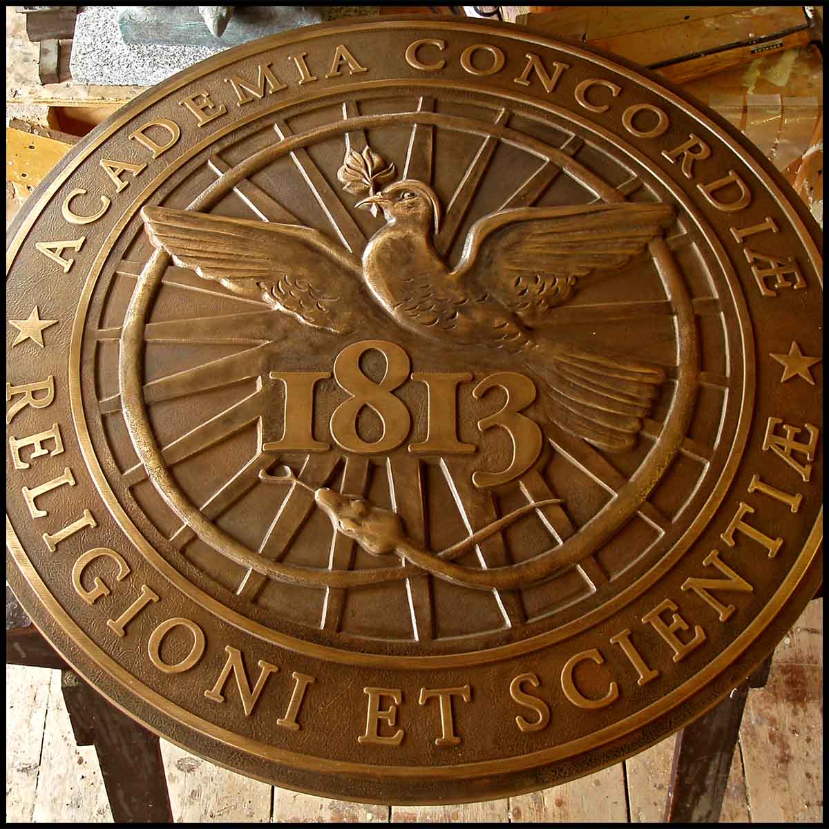 photo of bronze-colored sculpted relief of Kimball Union Academy seal featuring bird, snake, and Latin text in sculptor's studio