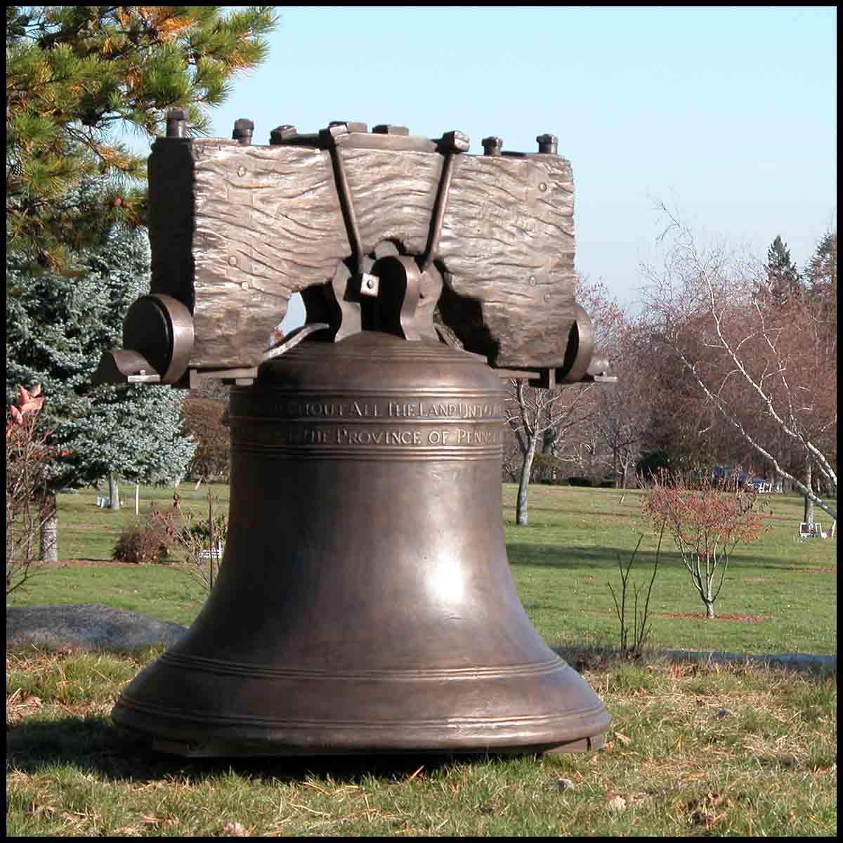 photo of bronze-colored Liberty Bell with yoke in field with trees in background