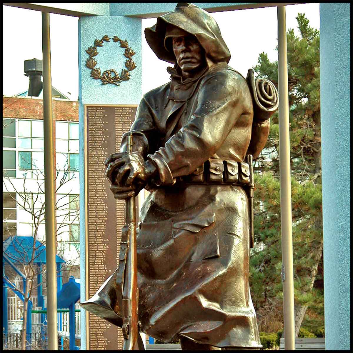 photo of bronze sculpture of male American soldier wearing hood and holding rifle at one end and resting it on ground surrounded by granite gazebo