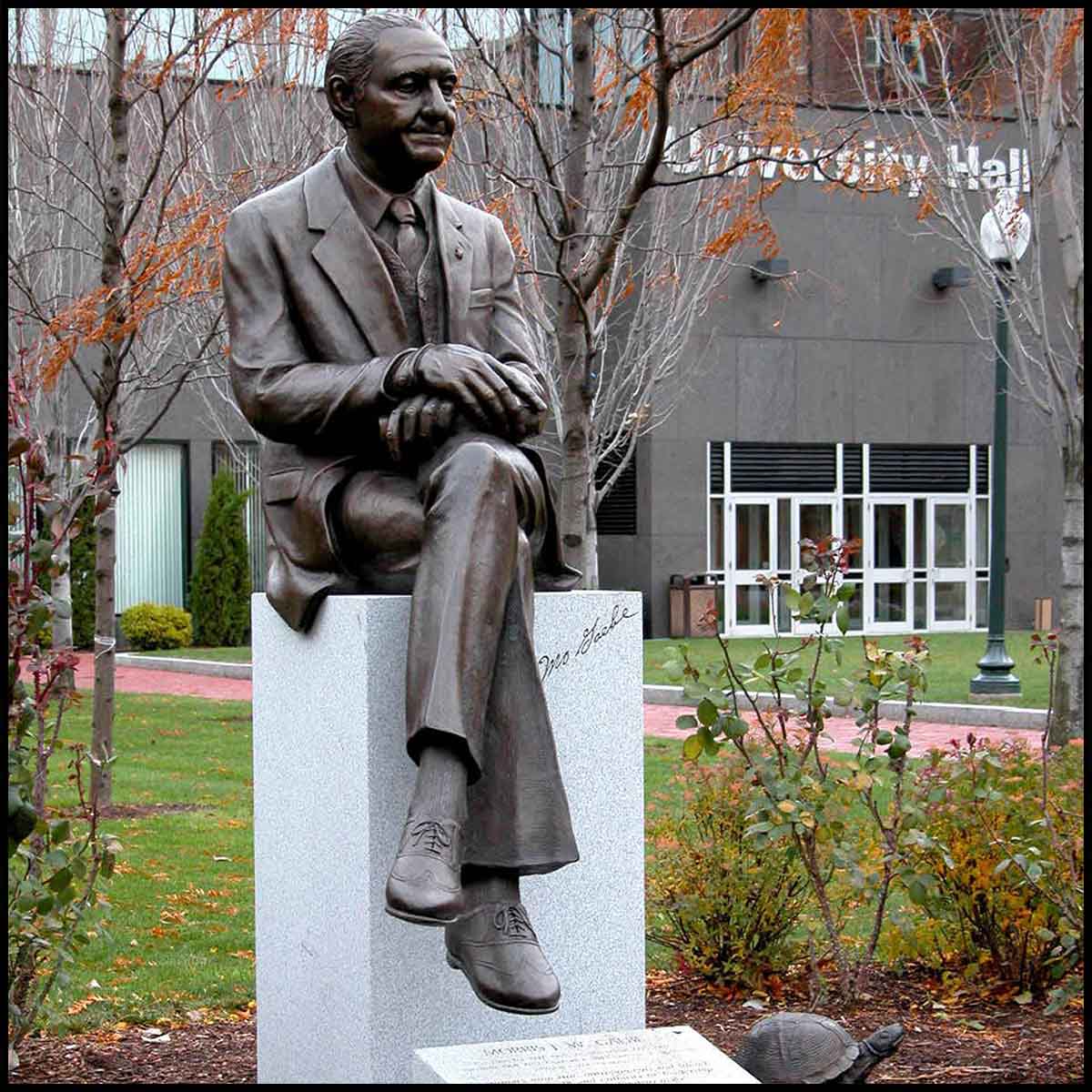 photo of bronze statue of Morris Gaebe sitting on stone base on college campus